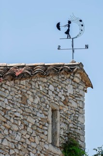 Weather vane on a stone roof under a blue sky, Provence, France
