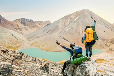 Aerial rising view young woman Hiker standing and watching beautiful alpine lake and mountains in