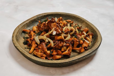 Chanterelle mushrooms are cooked with onion and herbs and placed on wooden plate. Dish shows golden