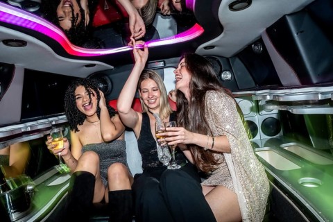 Happy young women enjoying a luxurious limousine party, laughing and dancing while holding