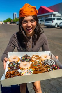 Woman standing outdoors on a sunny day, holding and offering a box filled with a variety of