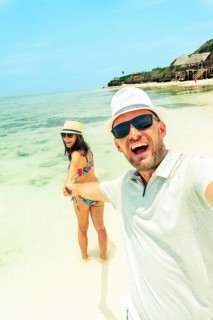 Happy couple takes a playful selfie while holding hands on a Zanzibar beach. Authentic joy and