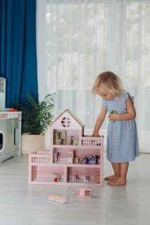 Child girl in blue dress arranges wooden furniture in a doll house. Concept of education during the