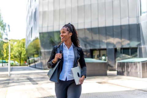 Pretty latin businesswoman walking holding laptop and handbag in a financial district