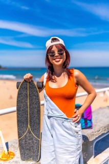 Vertical Portrait of a cool young female asian skater in summer modern clothes, cap and sunglasses