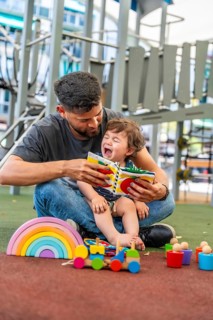 Father and tiny son sitting on soft ground in a playground, engaging in educational play with a