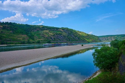 A river landscape with a narrow island surrounded by green hills and rocks under a blue sky with