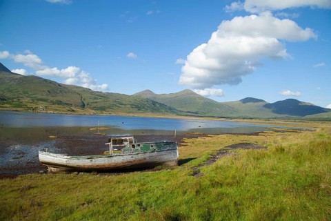 Derelict boat on the edge of a loch with a mountain landscape in the background, Isle of mull,
