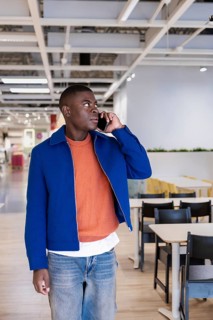 Smiling young African man talking on a smartphone in a modern store. He wears a blue jacket over an