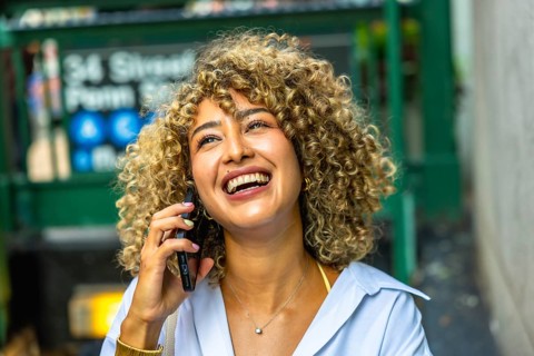 Young curly haired woman enjoying a phone conversation, laughing and smiling brightly while