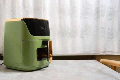 Air fryer on kitchen table next to window with sheer curtains. Simple and functional kitchen