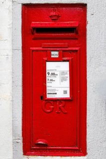 Red wall mounted Royal Mail postbox bearing the GR royal cipher, collection times displayed,