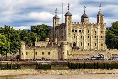 Visitors line the riverside path beside the Tower of London, where the pale turrets of the Norman