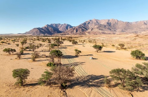 Aerial view of off-road car driving in dry riverbed and desert landscape on the Ugab River, behind