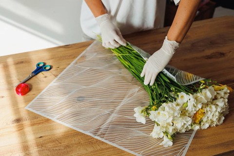 A person in gloves carefully arranges a bunch of fresh flowers, combining vibrant yellow and white