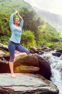 Woman in Hatha yoga balance yoga asana Vrikshasana tree pose at waterfall outdoors