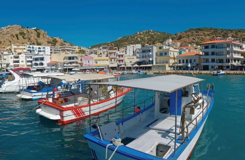 A harbour with boats in the foreground and colourful buildings on the shore, Karpathos Town,