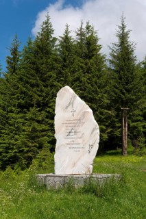 Monument stone surrounded by green trees and a meadow under a blue sky with clouds, Bratocea Pass,