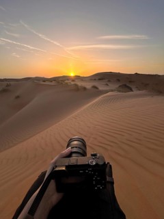 Cropped unrecognizable hand holding a camera towards the sunset over the rolling dunes of Wahiba