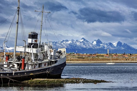 Ship in front of a coastal town with snow-capped mountains in the background and clouds in the sky,
