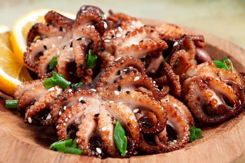 Grilled baby octopus with green onions, lemon slices, on a wooden plate, homemade, no people