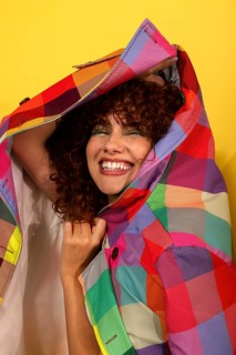 Cheerful woman with curly hair smiles brightly while draped in a vibrant, multicolored jacket. The