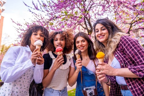 Four diverse female friends enjoying ice cream cones together on a sunny spring day under beautiful