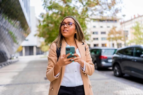 Frontal view of a latin woman using phone distracted walking along the city