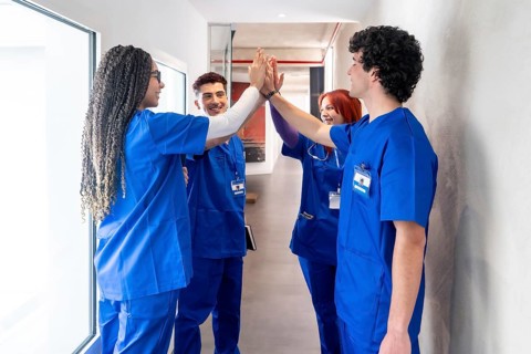 Young medical team members wearing blue scrubs and id badges are celebrating a successful moment by