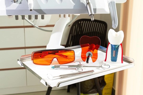 On the tray are various dental instruments, a model dental implant and bright orange safety