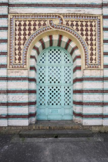 Metal door with decorations, patterns and bars, brick building with red, turquoise and white