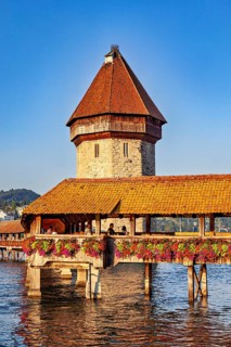 Medieval wooden bridge with tower and blooming flowers over a body of water in sunny weather, The