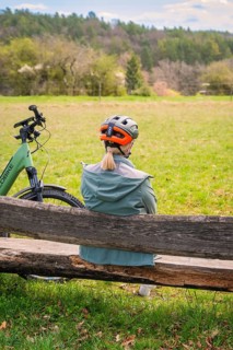 Person sitting on a bench at the edge of the forest, next to a bicycle, spring-like weather,