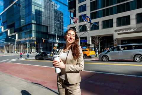 Young professional businesswoman smiling, confidently holding a reusable coffee cup while standing