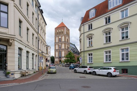 Paved road with flanking old town houses and church tower in the background under cloudy sky, St.