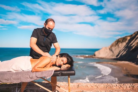 Massages on the beach on the coast near the sea, masseuse with face mask in the coronavirus