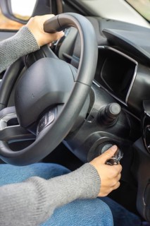Close-up of hands starting a car, one on steering wheel and one turning key in ignition, car