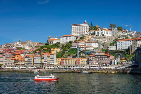 Tourist boat crosses the Douro River in Porto, Portugal, below Ribeira riverfront and the historic