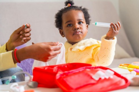 Close-up of a cute african girl playing with emergency kit toy with her mother