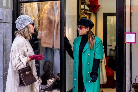 Young blonde girl enjoying shopping in the city and being attended by a shop assistant, looking at