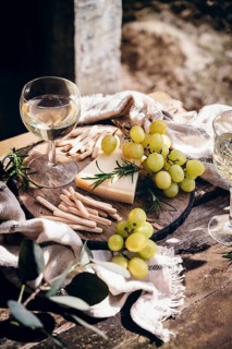 A elegant outdoor still life featuring a glass of white wine, green grapes, rosemary and cheese on