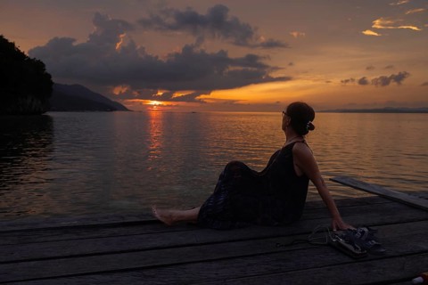 A mature female tourist relaxes on a wooden pier on Kri Island in the Raja Ampat Archipelago,
