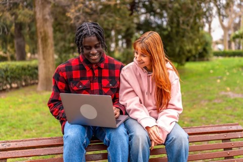 Two college students collaborating on a project, using laptop in a park, enjoying the pleasant