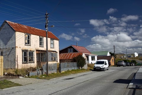 Small village street with old and new houses, cars parked, under a clear blue sky, Stanley, East