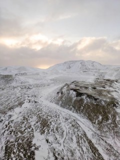 Aerial view of Iceland's winter landscape, showcasing snow-covered hills and distant mountains
