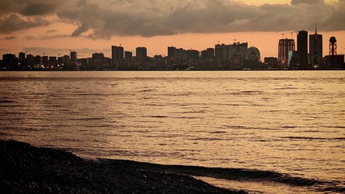 Melancholy cityscape at dusk with a view of a quiet river and pebble beach, Batumi, Georgia