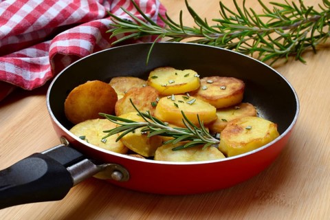 Fried potatoes in pan with rosemary sprig