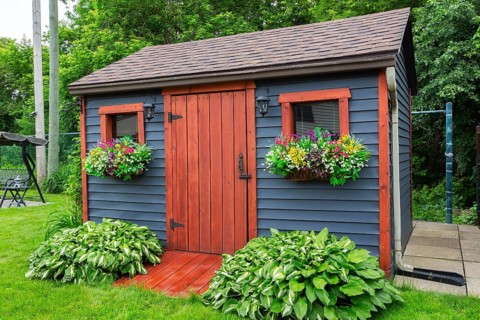 Dark grey clapboard cladded garden storage shed with cedar wood plank door and window flower boxes