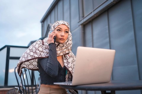 Arab girl with a white veil at the computer on the terrace of a coffee shop, with the computer and