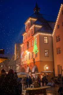 Christmas-lit old town buildings at a winter market at night, people strolling in the snow,